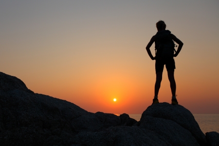 Hiker with backpack standing on top of a mountain and enjoying sunsetの写真素材