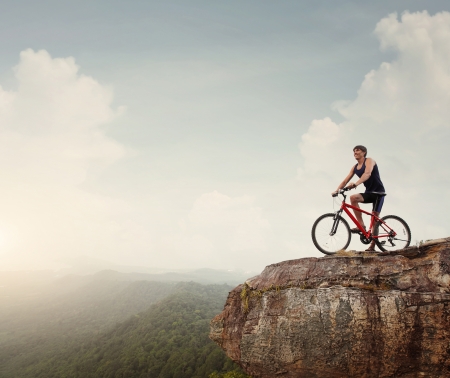 Young athlete standing on top of a mountain with bicycle and enjoying valley viewの写真素材