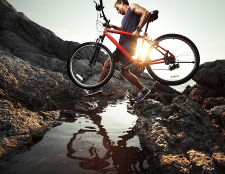 Young athlete crossing rocky terrain with bicycle in his handsの写真素材