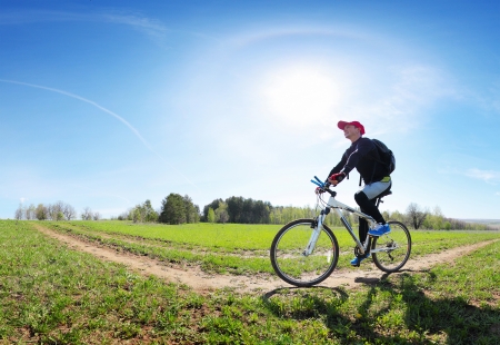 Young man cycling on a rural road through green spring meadow at sunny dayの写真素材