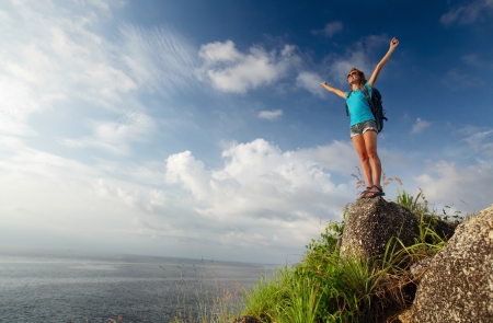 Hiker with backpack and raised hands enjoying sunset over seaの写真素材