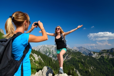 Young ladies with backpacks taking a pictures with Alps on the backgroundの写真素材
