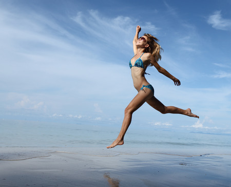 Woman jumping and running on a sandy beachの写真素材