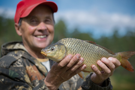 Happy mature fisherman holding his trophy carp (Cyprinus carpio). Focus on the fishの写真素材