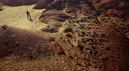 Woman with bicycle crossing desert with rocksの写真素材