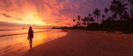 Lady walking on the wet sandy beach during sunset