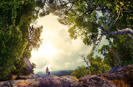 Hiker with backpack standing on the rock surrounded by lush tropical forest
