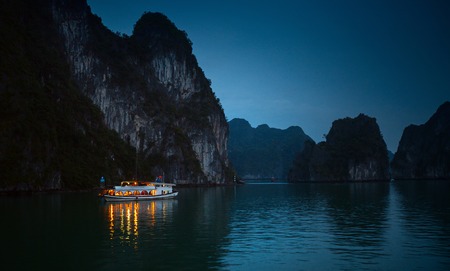Illuminated boat anchored in the calm Ha Long Bay   near the limestone mountain.の写真素材