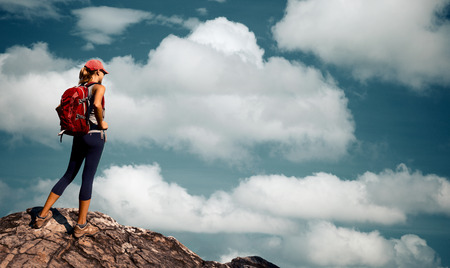 Lady hiker standing on top of the mountain on the sky background full of fluffy cloudsの写真素材