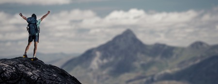 Hiker with backpack standing on top of the mountain with raised handsの写真素材