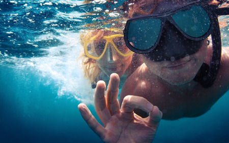 Young couple having fun underwater and showing ok signの写真素材