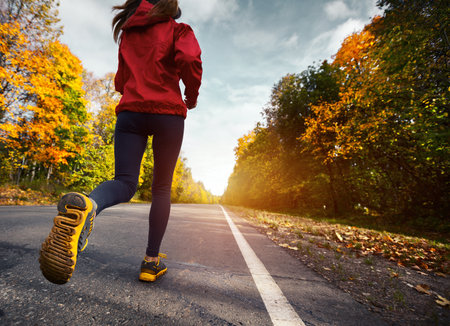 Lady running on the asphalt road through the autumn forestの写真素材