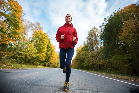 Lady running on the asphalt road through the autumn forestの写真素材