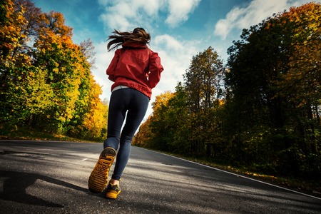 Lady running on the asphalt road through the autumn forestの写真素材