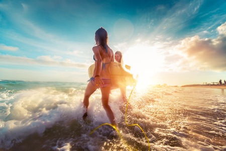 Two ladies running into the sea with surf boards at sunset