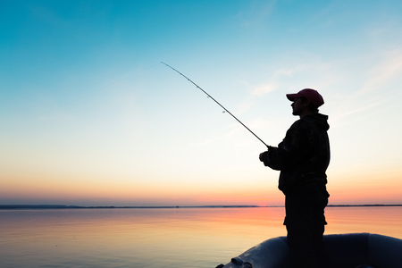 Man fishing from the boat on the lake at sunsetの写真素材