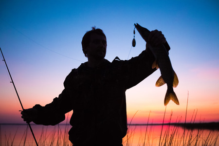 Silhouette of the fisherman with fish and lureの写真素材
