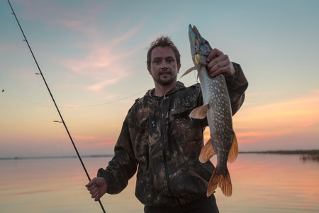 Man holding trophy fish with the sunset lake on the background