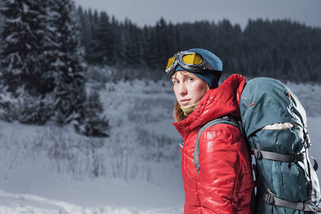 Young woman with goggles looking to a camera with winter forest on the backgroundの写真素材