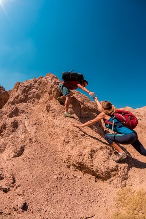 Two hikers crossing rocky terrain in the desert at sunny dayの写真素材
