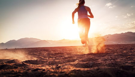 Young lady running on the desert at sunsetの写真素材