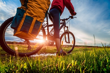Hiker with loaded bicycle on a green summer meadow at sunsetの写真素材
