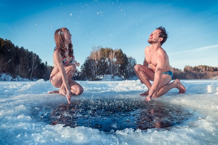 Young couple having fun and splashing the water of a winter lakeの写真素材