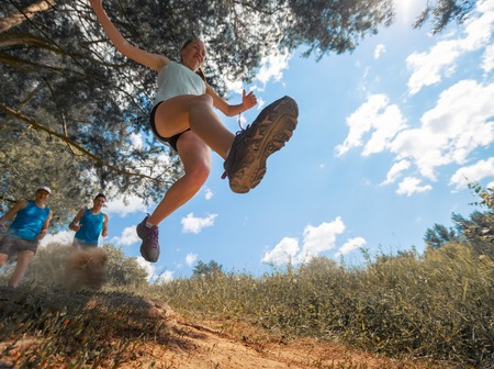 Trail running athlete jumping over camear at sunny day