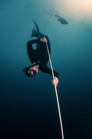 Free diver descending along the rope in the depthの写真素材