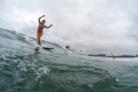 INDONESIA, BALI, CANGGU - NOVEMBER 25 2016: Young lady surfer catching the wave in the ocean