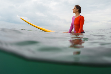 Underwater split shot of the young lady surfer sitting on a board awaiting the waves
