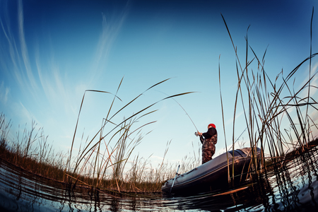 Man fishing from the boat on the lake at sunsetの写真素材