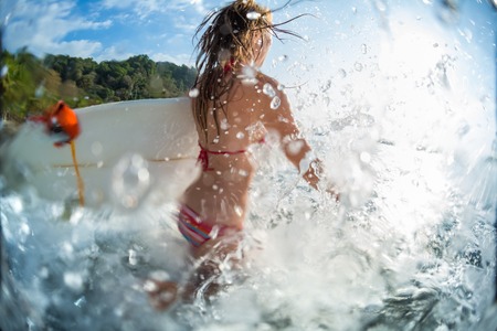 Woman runs into the sea with surfboard and lots of splashesの写真素材