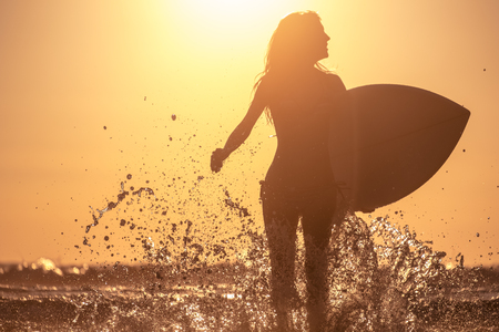 Young woman runs with surfboard with lots of splashes