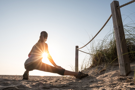 Woman performs stretching exercises on a beach at sunrise
