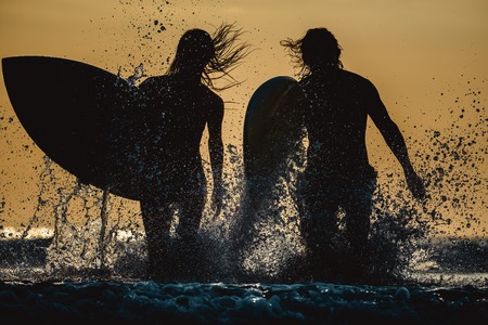 Couple of surfers run with boards and lots of splashesの写真素材