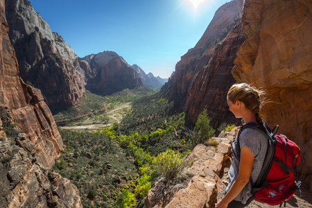 Young woman hiker with backpack stands on the edge and looks down at the valley of Zion National Park, Angels Landing trail, USAの写真素材