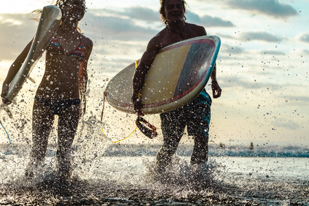 Couple of surfers run with boards and lots of splashes