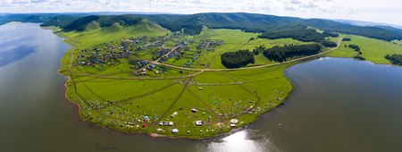 Aerial view of the outdoor festival with camping tents and other buildings set on the green coast of a lakeの写真素材