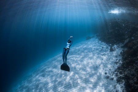 Woman freediver glides over sandy bottom of a crystal clear tropical seaの写真素材