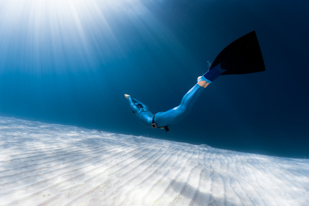 Woman freediver glides over sandy sea bottomの写真素材