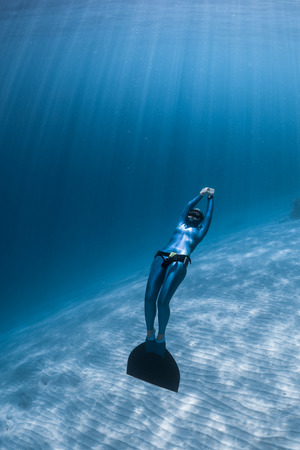 Woman freediver relaxes underwater with monofin over sandy bottomの写真素材