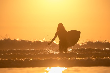 Woman with surfboard runs from the ocean with lots of splashesの写真素材