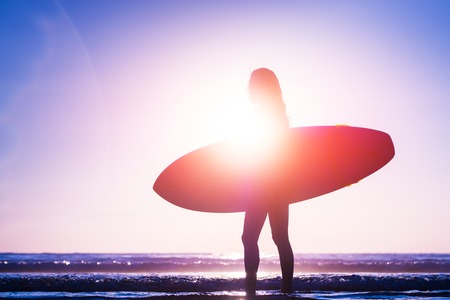Woman with surfboard walks on the beach during sunsetの写真素材