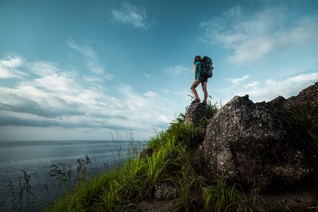 Lady hiker with backpack standing on the stone and enjoying sea viewの写真素材