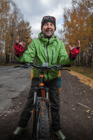 Mature bicycle tourist with his loaded bike on an asphalt autumn roadの写真素材