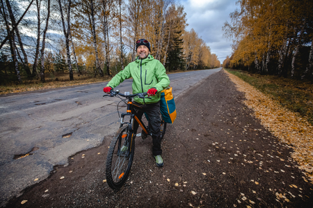 Mature bicycle tourist with his loaded bike on an asphalt autumn roadの写真素材