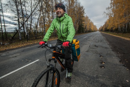 Mature bicycle tourist with his loaded bike on an asphalt autumn roadの写真素材