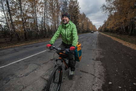 Mature bicycle tourist with his loaded bike on an asphalt autumn roadの写真素材