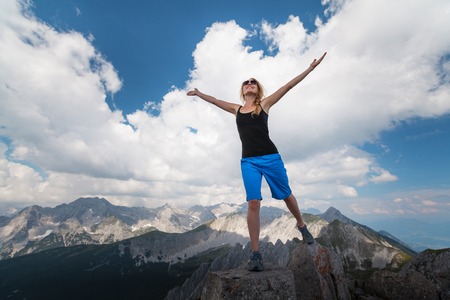 Young lady standing on top of the hill with raised handsの写真素材